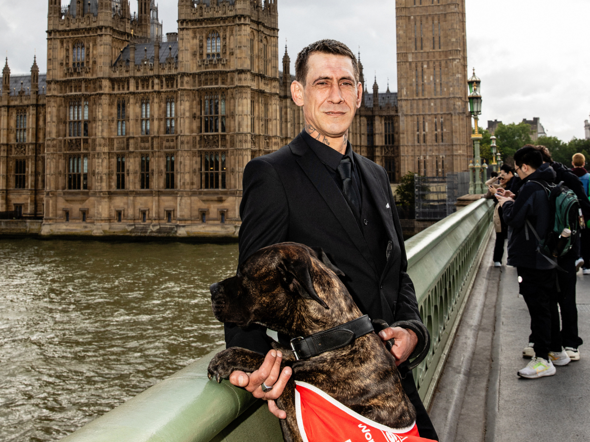 Big Issue vendor Andy stands with his dog Charm on Westminster bridge with parliament in the background