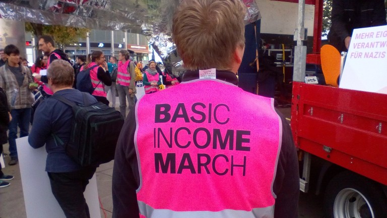 A person wearing a hi-vis jacket reading 'Basic Income March'