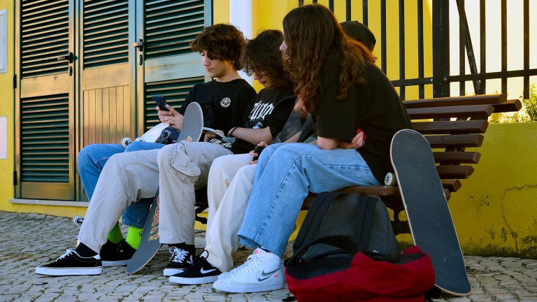 young people with skateboards sat around on phones