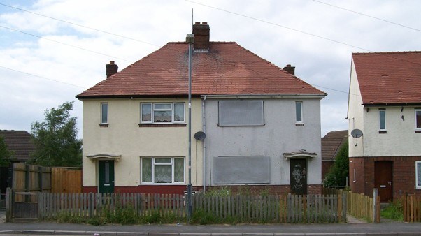 A pair of semi-detached homes, one side is empty and boarded up