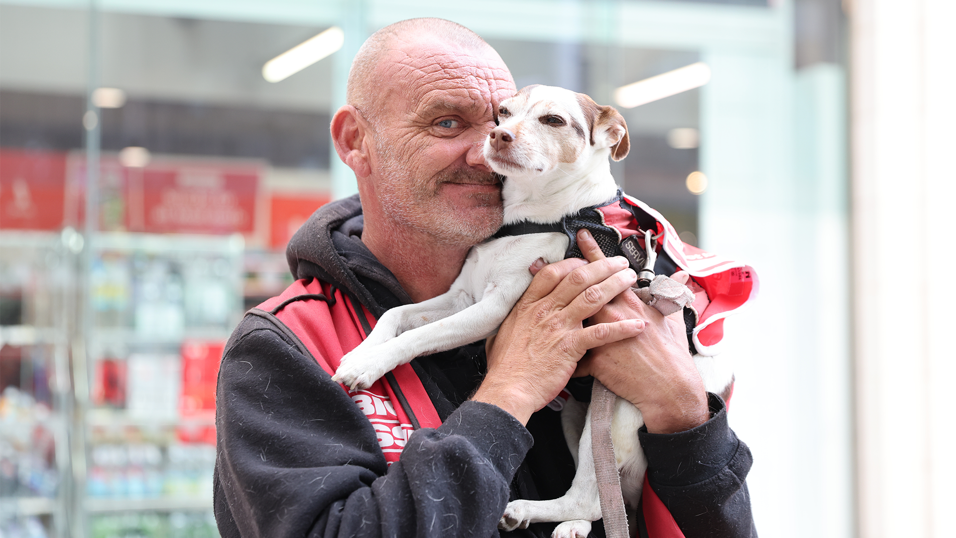Big Issue vendor Robin Price cuddles his Jack Russell, Tinks both wearing their red Big Issue tabards