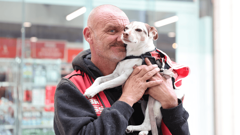 Big Issue vendor Robin Price cuddles his Jack Russell, Tinks both wearing their red Big Issue tabards